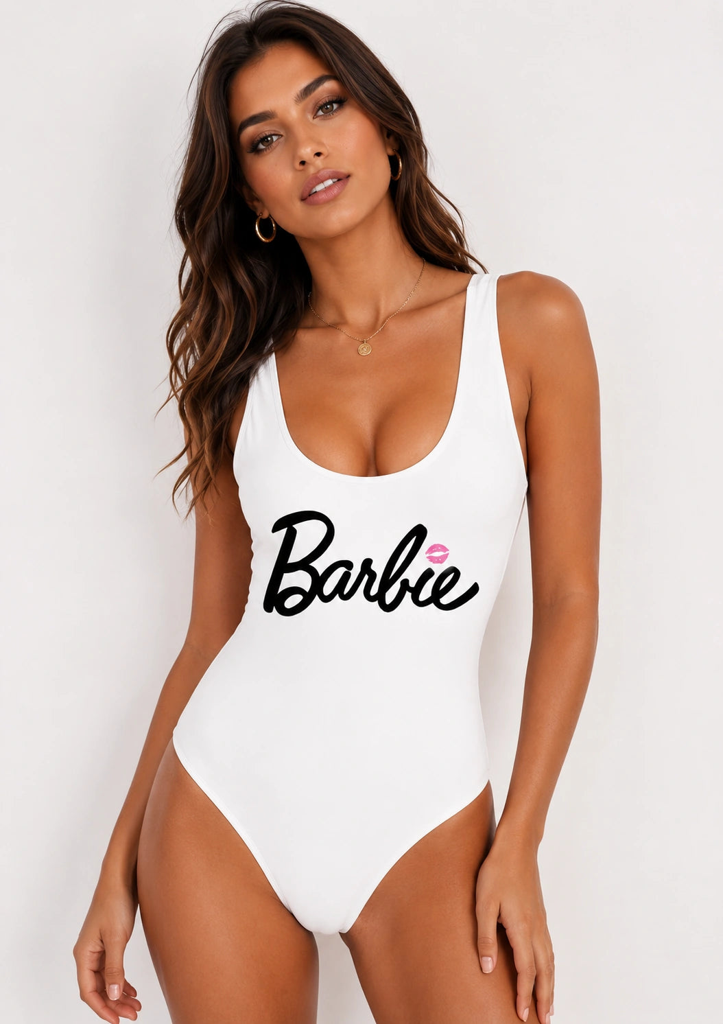A woman modeling a white one-piece swimsuit with a black 'Barbie' script logo and a small pink heart accent on the chest, set against a plain light background.