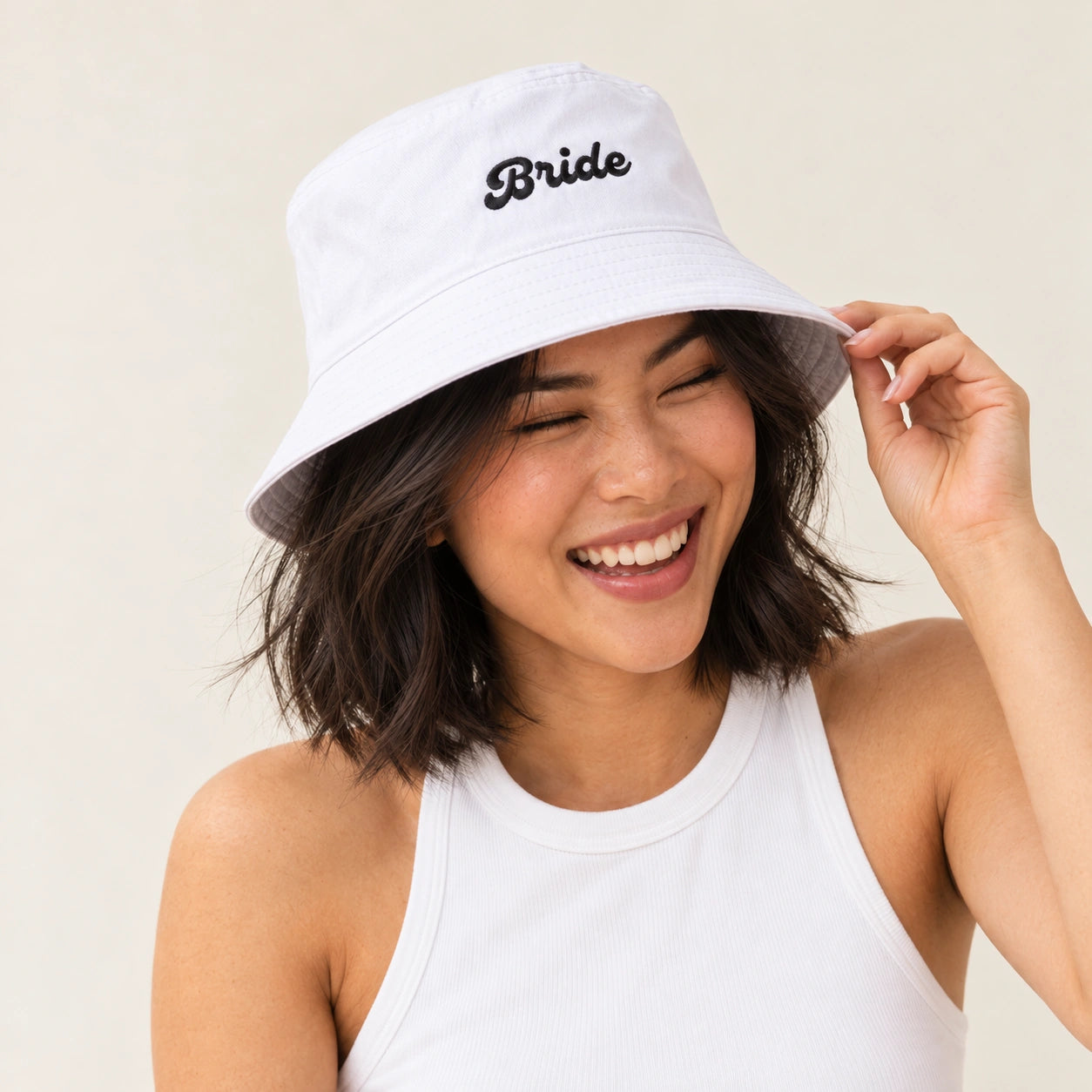 A woman wearing a white bucket hat with 'Bride' black script on the front, posing against a light beige background.