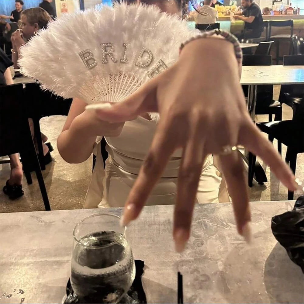 Person holding a decorative fan with 'Bride' on it in a restaurant setting.