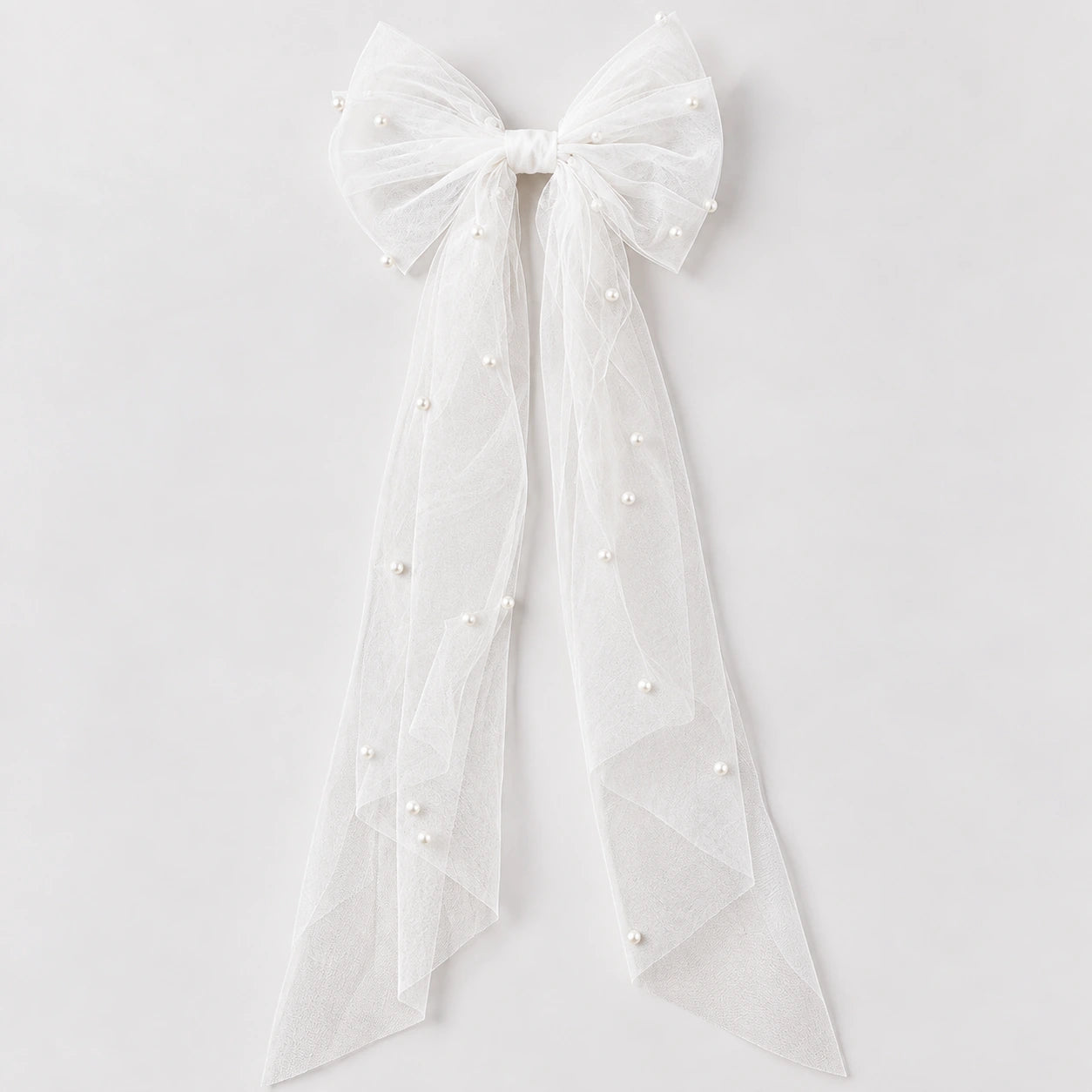 White tulle bow hair accessory with long ribbon tails and small pearl embellishments, shown against a light gray background.