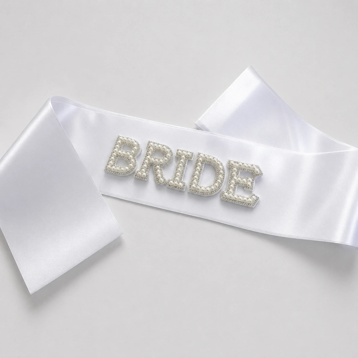 White satin bride sash with pearl embellished BRIDE lettering on a clean studio background.