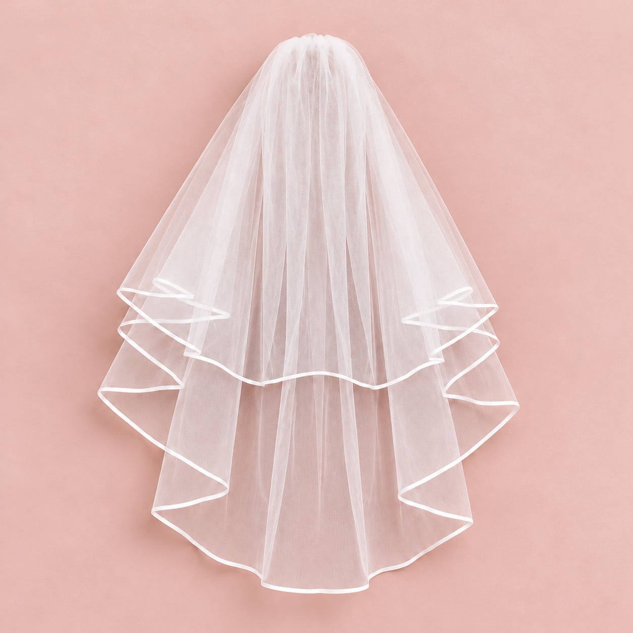 Two-tier sheer white bridal veil with curled ribbon edging on a blush pink background.