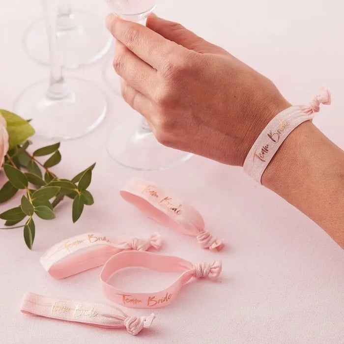 Pink 'Team Bride' wristbands for hen party celebrations with wine glasses and greenery